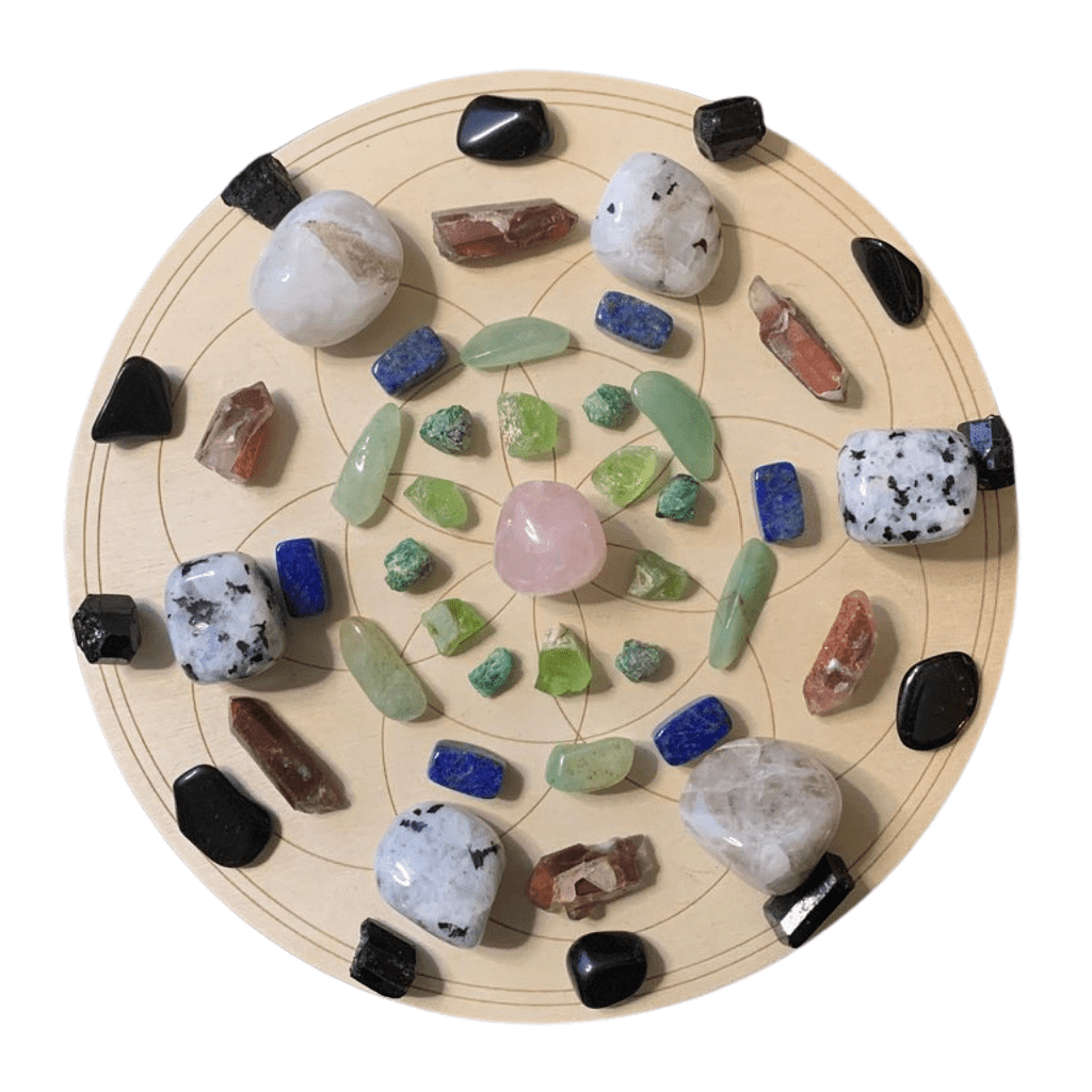 A Seed of Life crystal grid displayed on a wooden board. A rose quartz stone is placed in the centre, surrounded by layers of aventurine, peridot, lapis lazuli, rainbow moonstone, and black tourmaline. The crystals are arranged symmetrically in circular layers, creating a vibrant, harmonious energy pattern.