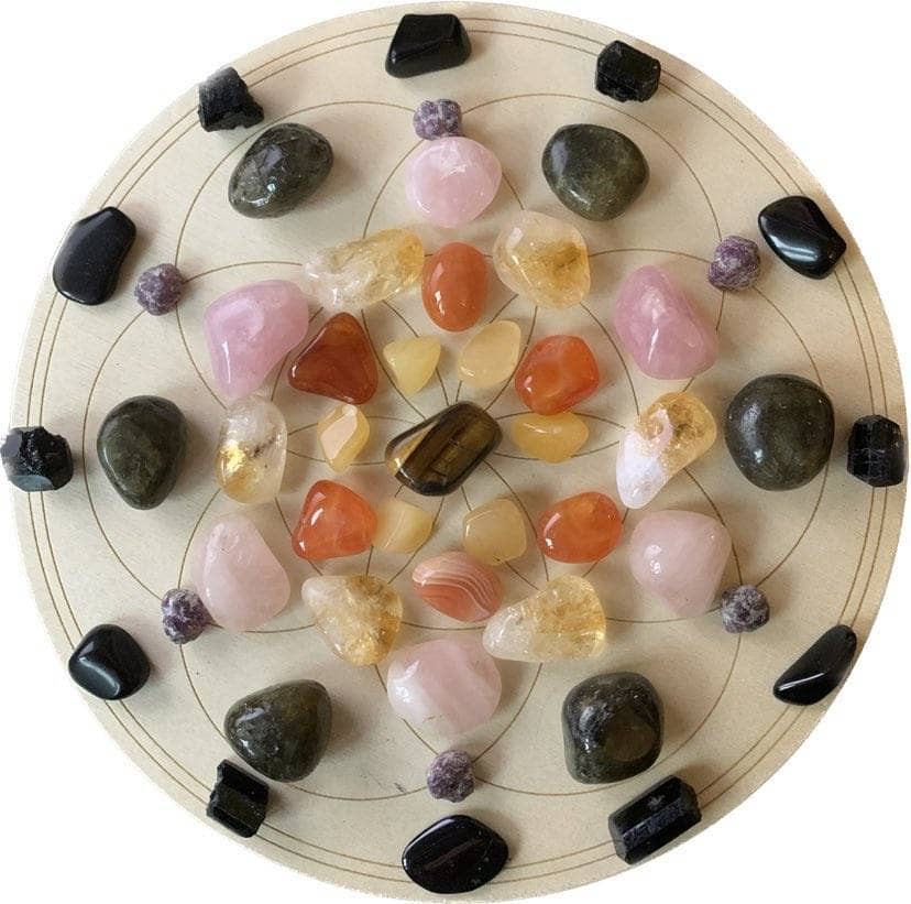 A circular crystal grid featuring a central tiger's eye surrounded by citrine, carnelian, yellow aventurine, rose quartz, labradorite, black tourmaline, on a Flower of Life pattern.